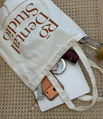 Flat lay of a tote bag with dental studio branding, containing a phone, notebook, and small accessories.