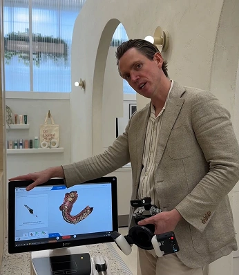 Dentist holding a camera and showing a digital 3D dental scan on a computer screen in the clinic.