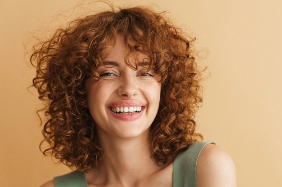 A smiling woman with curly hair showcasing a bright, confident smile at Rō Dental Studio